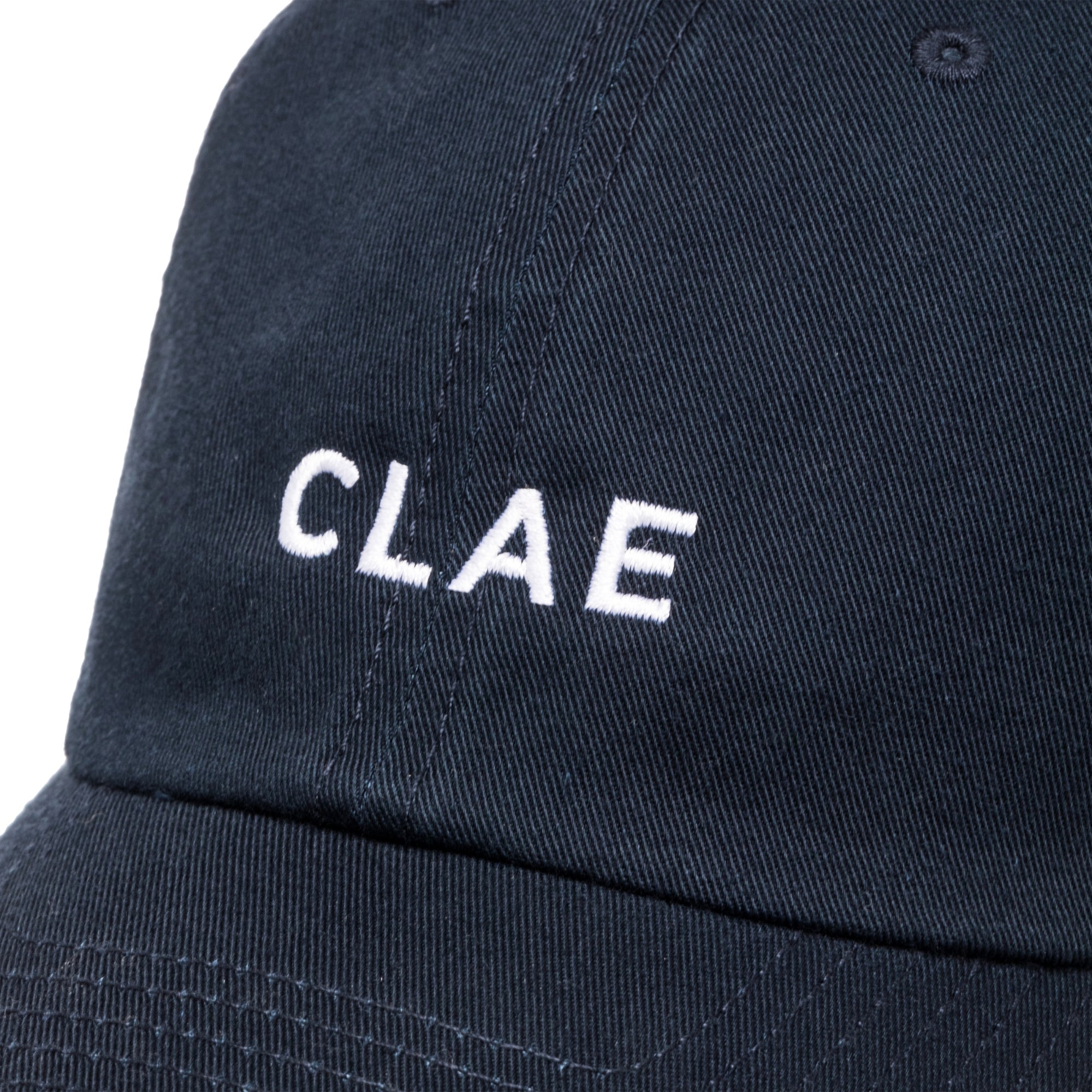 Close-up of white CLAE embroidery on navy cotton dad hat